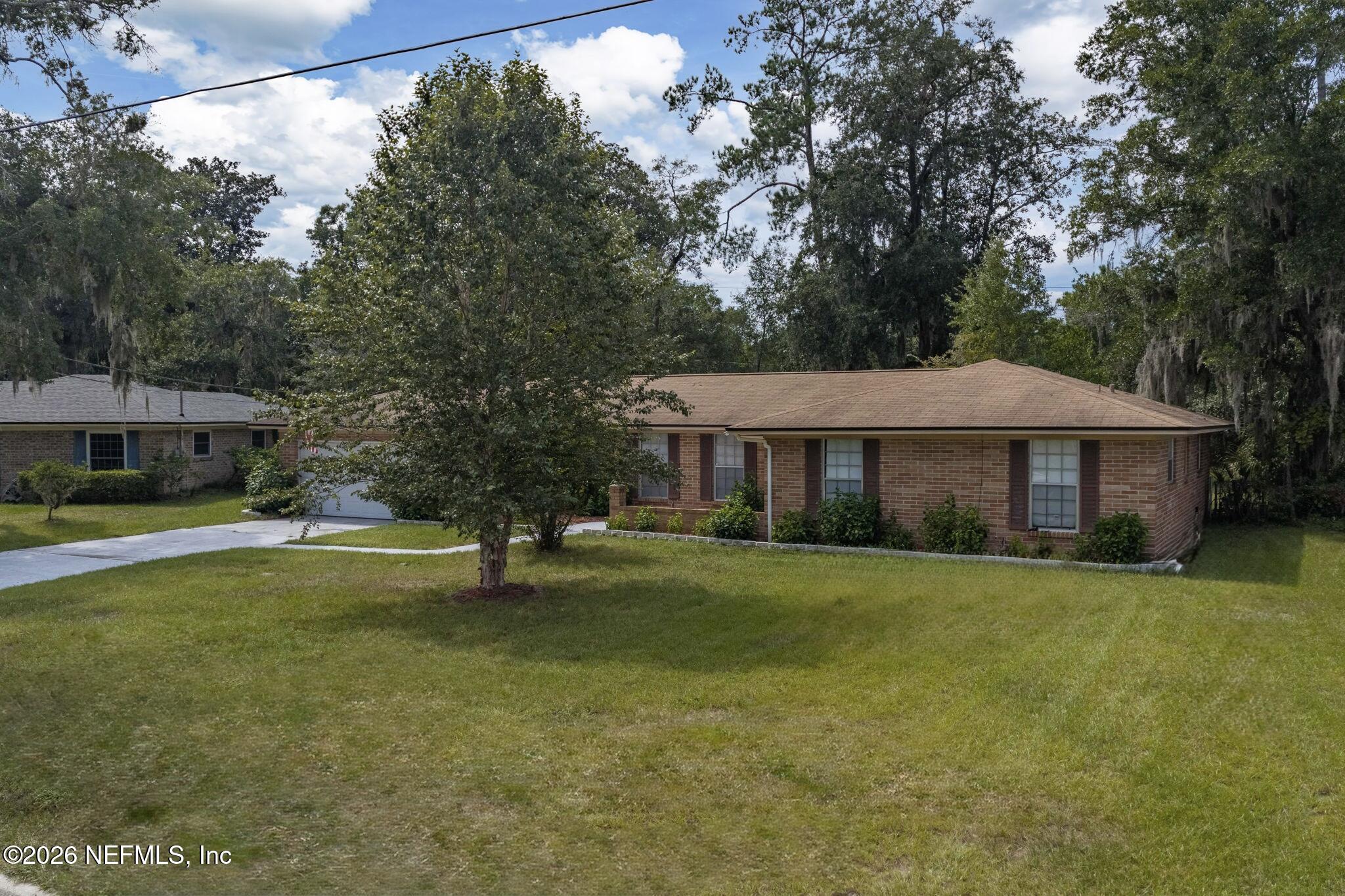 Single-story brick house with a broad lawn, driveway, and mature trees.