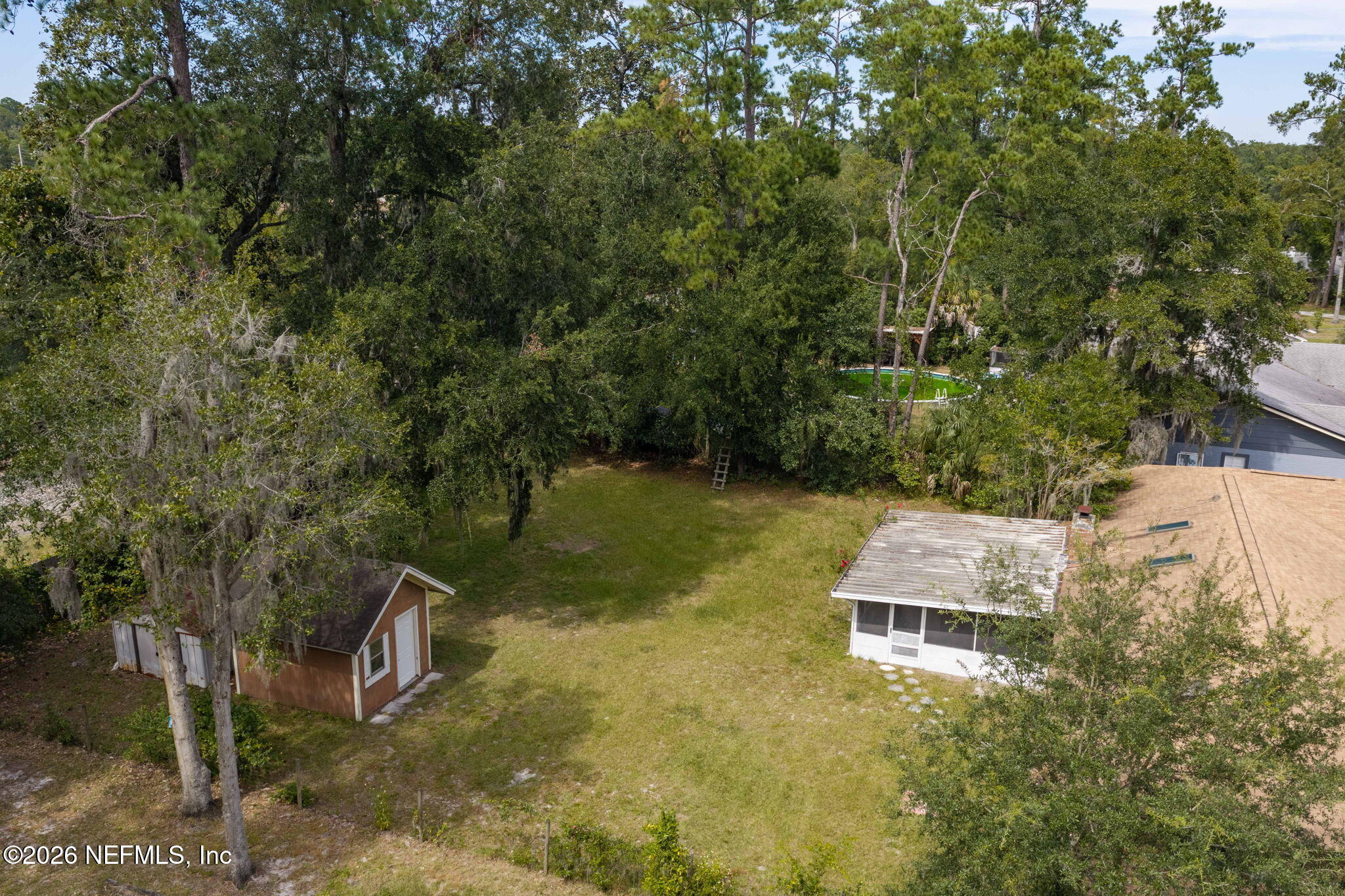 Aerial view of a tree-lined backyard with a brown shed, screened patio, and partially visible pool.