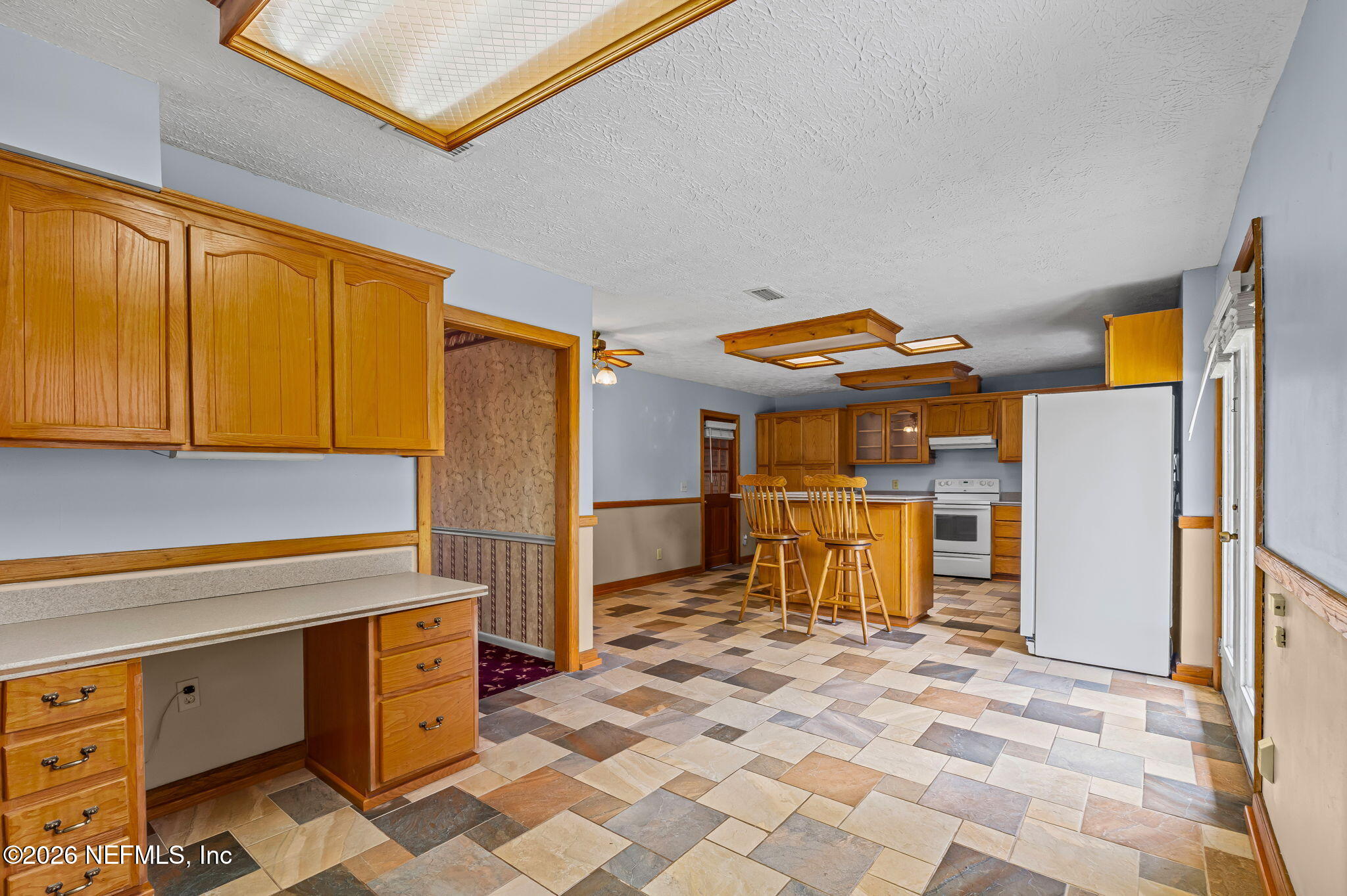 Kitchen with honey-colored wood cabinets, an island with two stools, and patterned tile flooring.