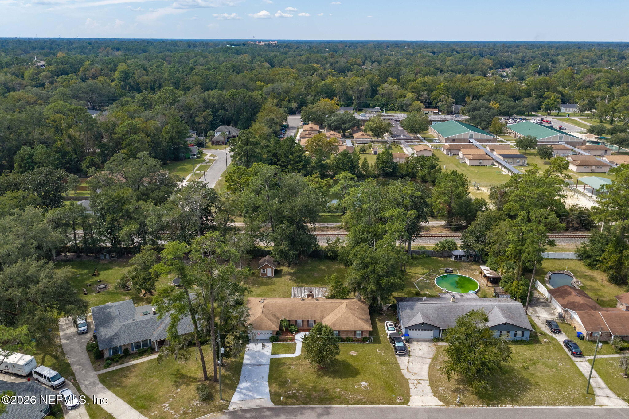 Aerial view of a single-story home with a broad lawn, neighboring houses, and railroad tracks behind it.