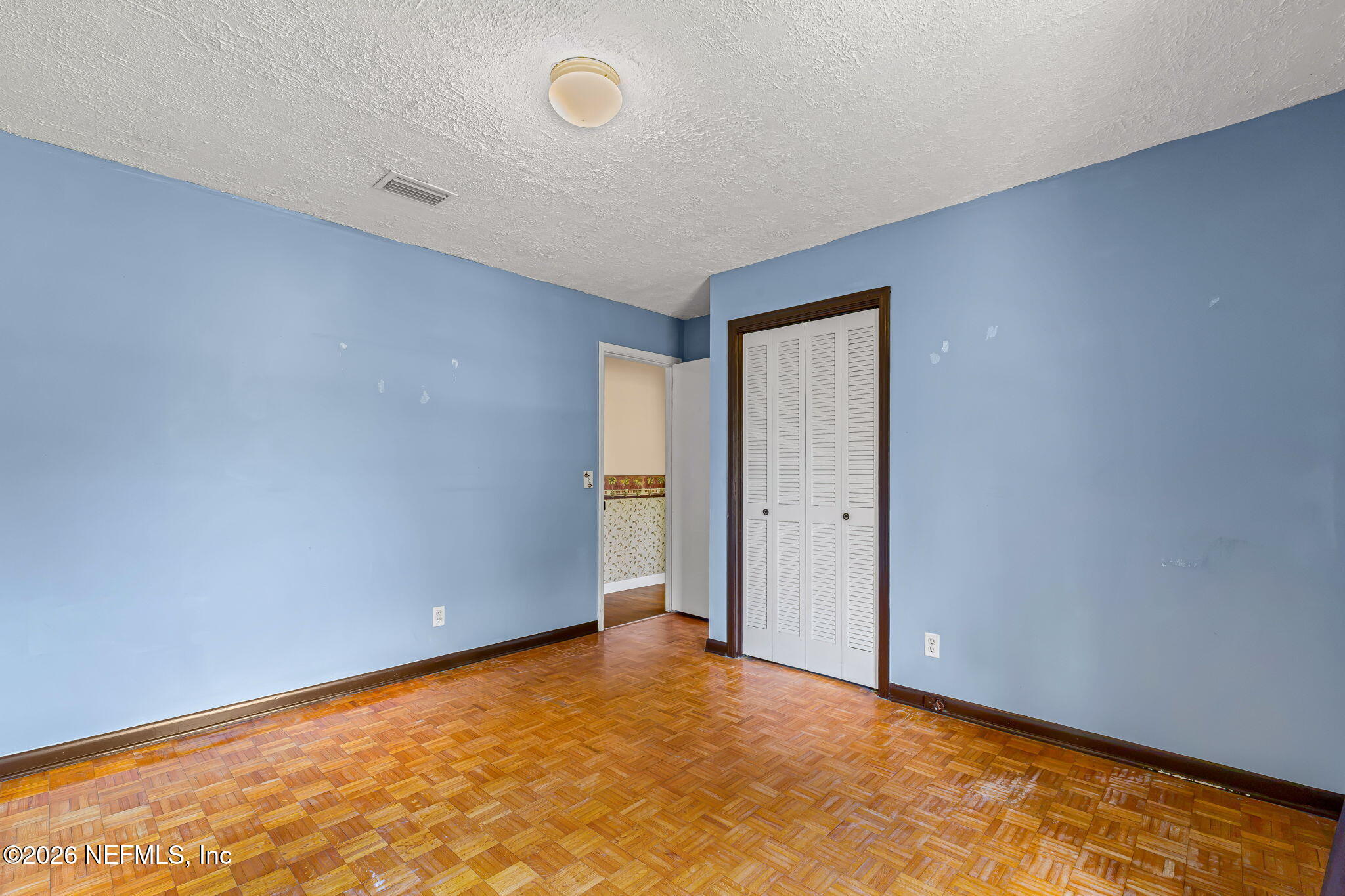 Vacant bedroom with blue walls, parquet flooring, and a louvered closet.