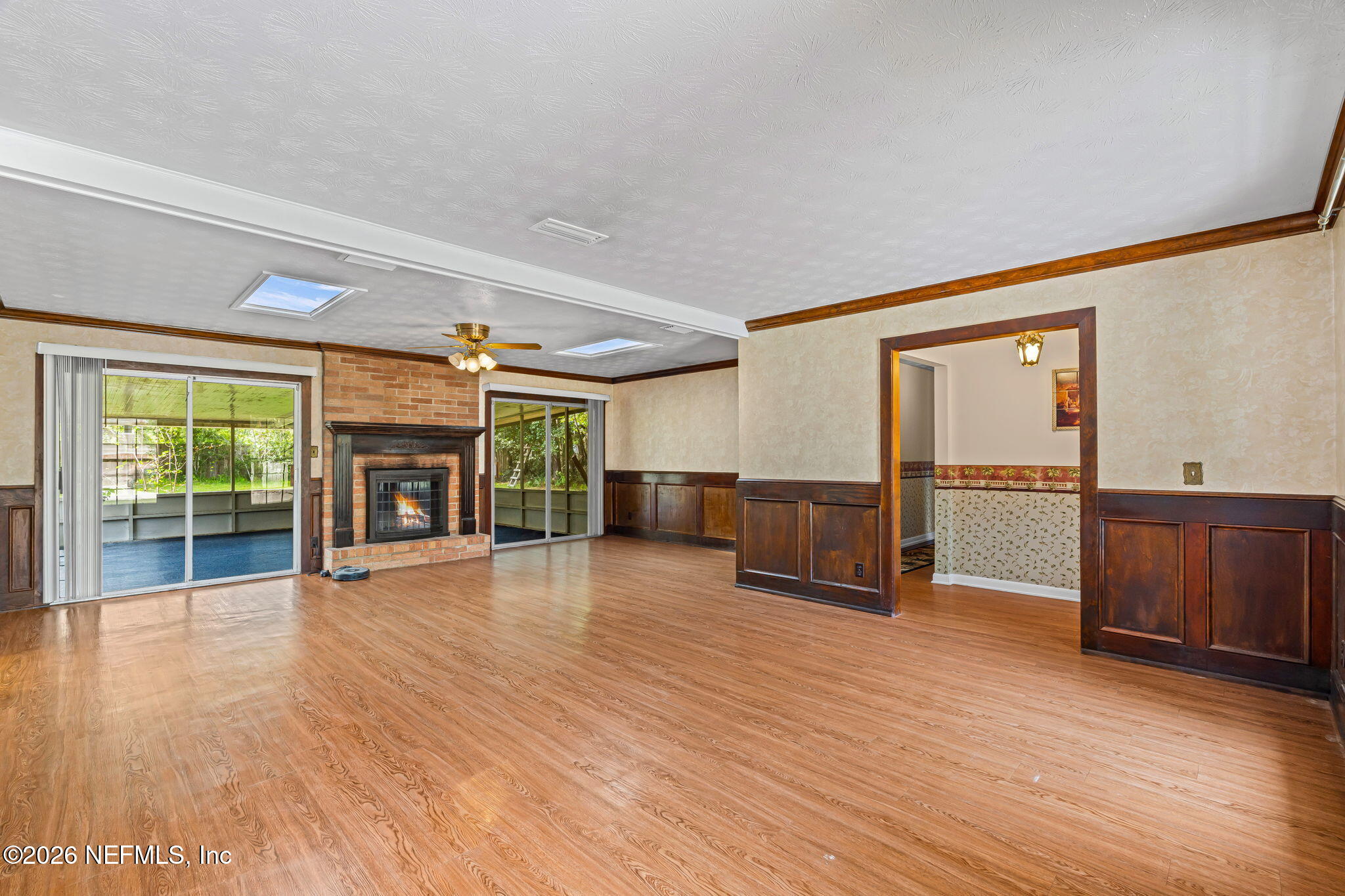 Vacant living room with a brick fireplace, hardwood floors, skylights, and sliding glass doors.