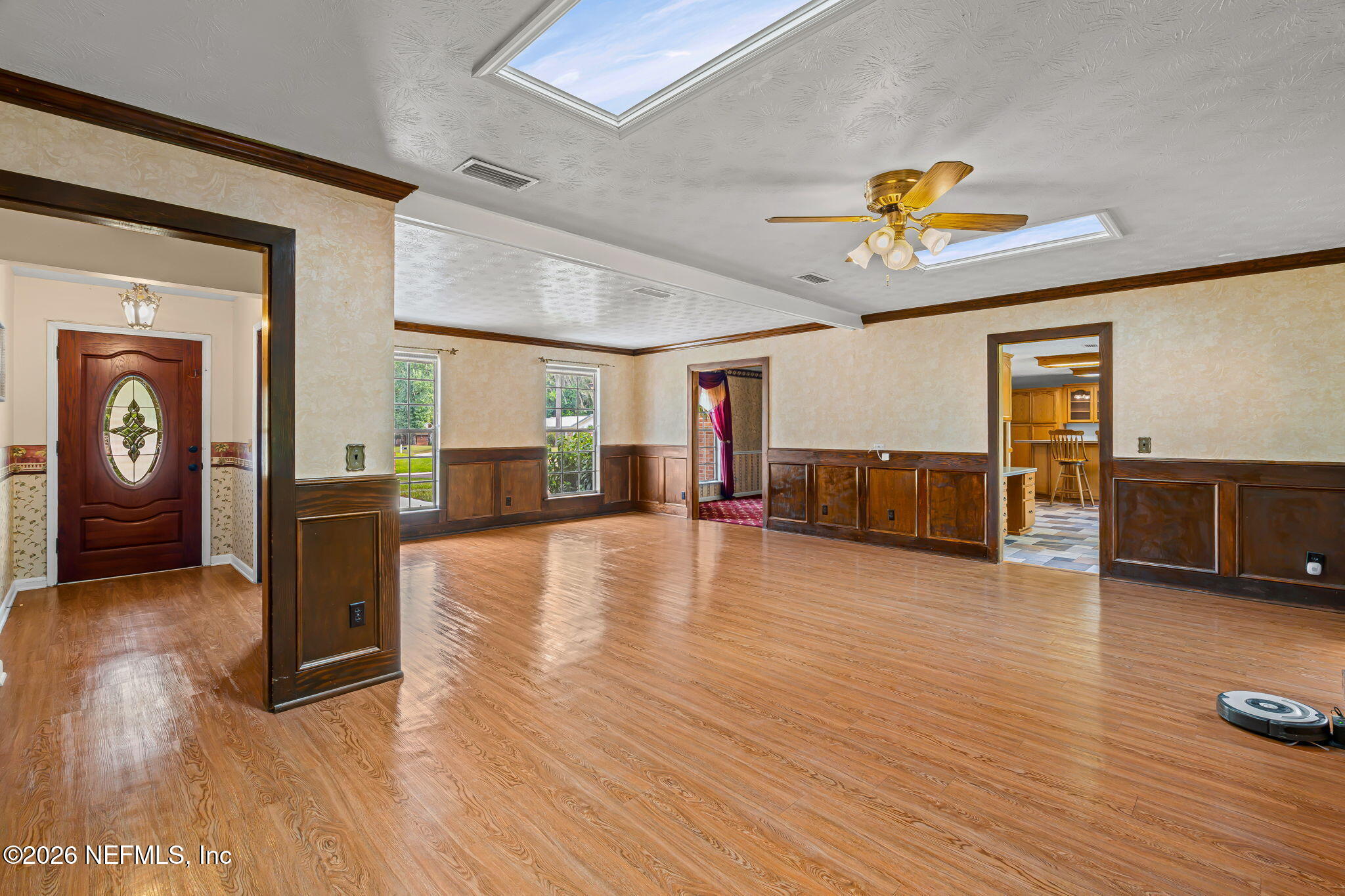 Vacant living room with polished wood floors, dark wood paneling, and two skylights.