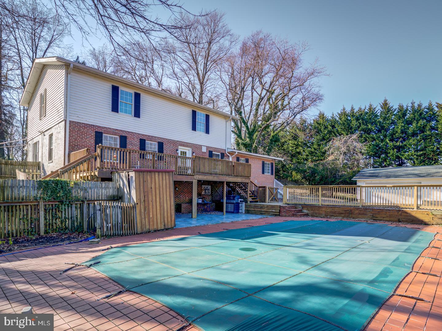 Rear of a brick-and-siding home with a raised deck overlooking a covered pool and brick patio.