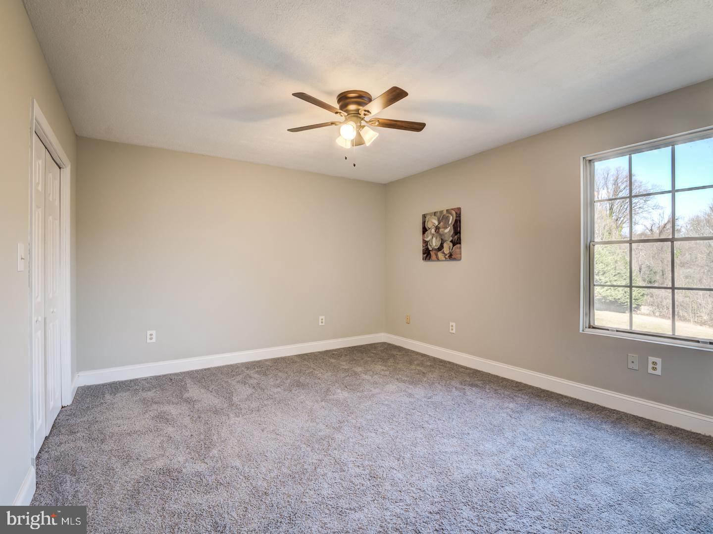 Unfurnished bedroom with gray carpet, ceiling fan, and a large window overlooking trees.