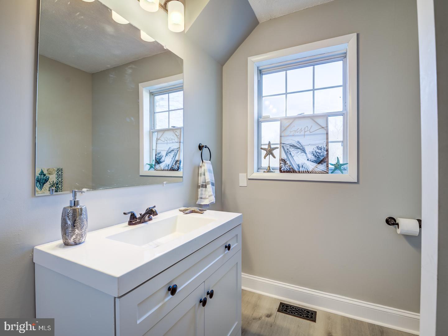 Bathroom with a white vanity, large mirror, and window decorated with coastal accents.