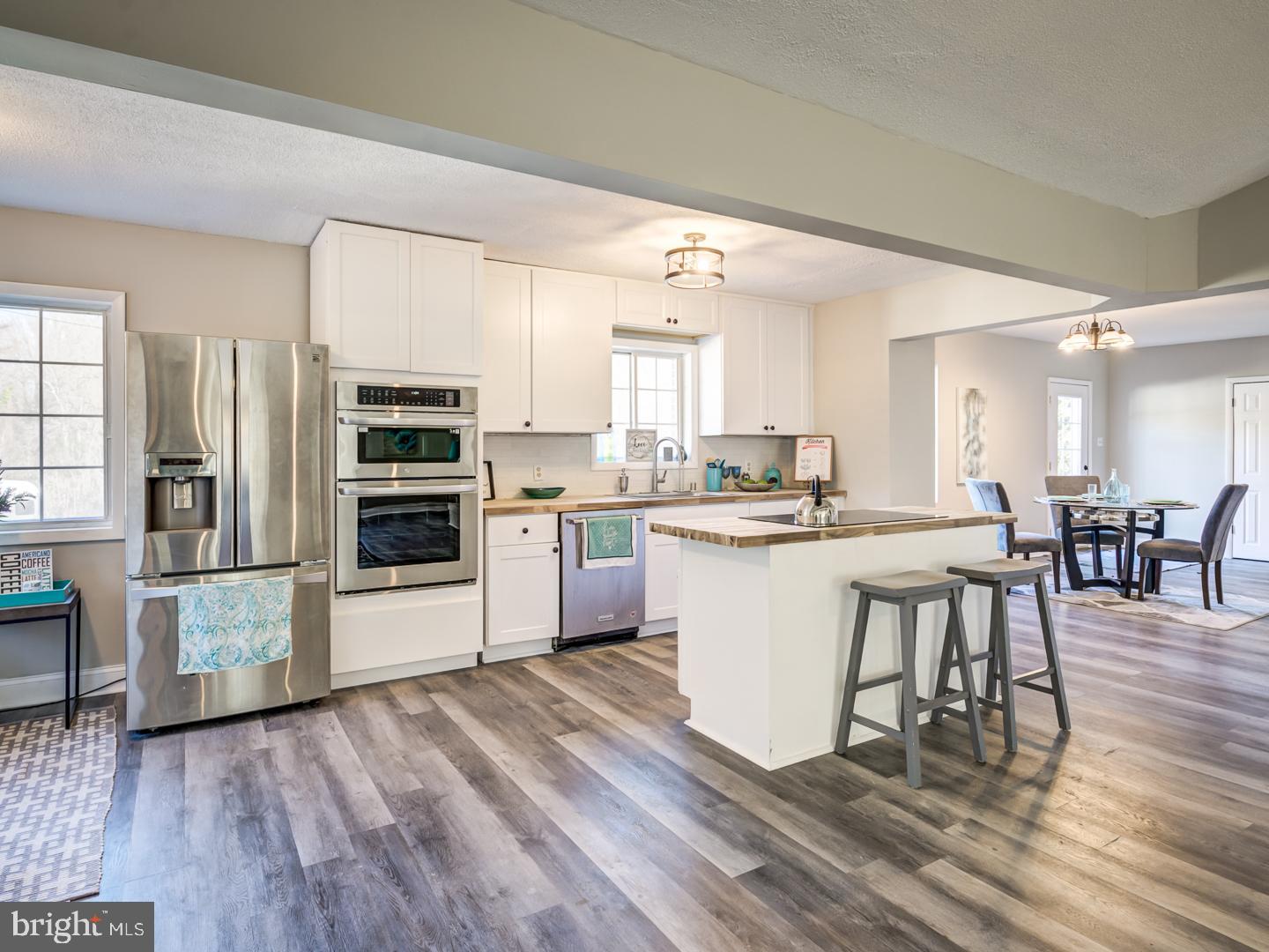 Open kitchen with white cabinets, stainless steel appliances, and an island with bar stools.