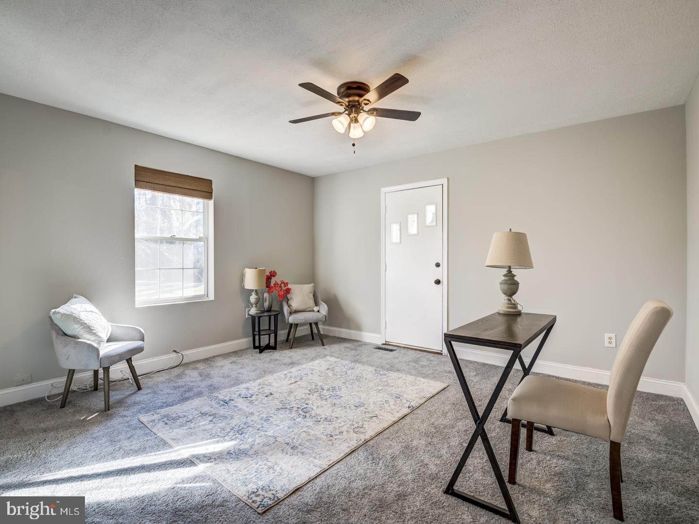 Furnished room with gray carpeting, a patterned rug, two chairs, and a narrow table.