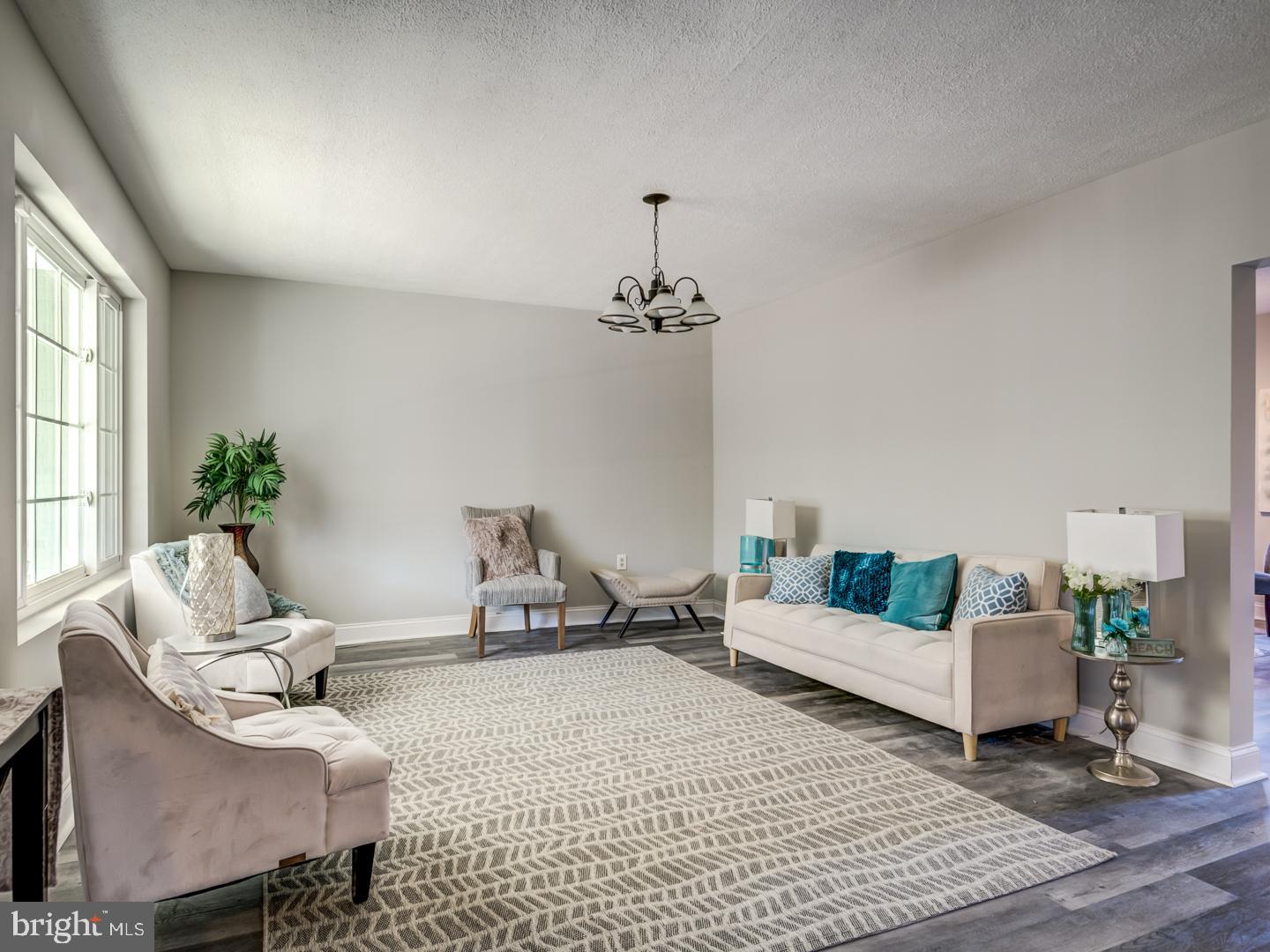 Staged living room with a white sofa, teal pillows, and tall windows.