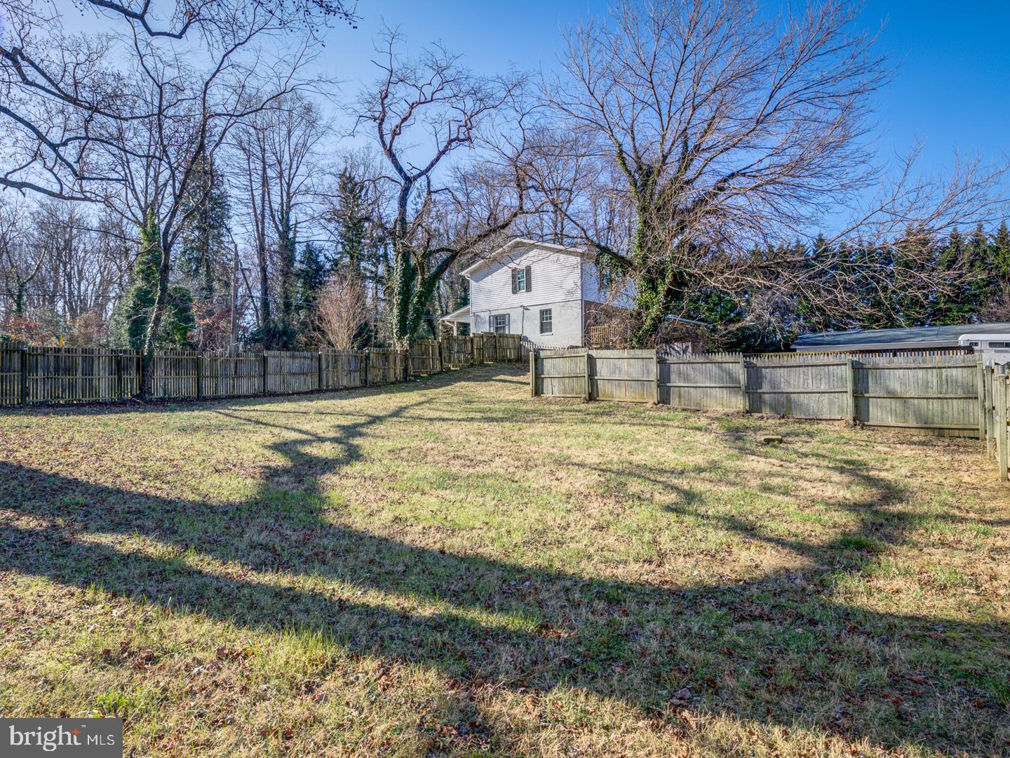 Fenced grassy yard behind a two-story house, with leafless trees and a detached outbuilding.
