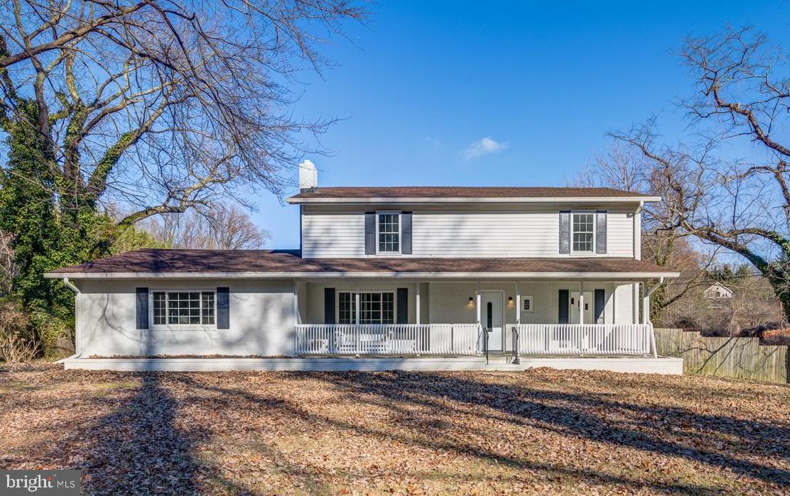 Two-story white house with a long covered porch and white railings, framed by bare trees.