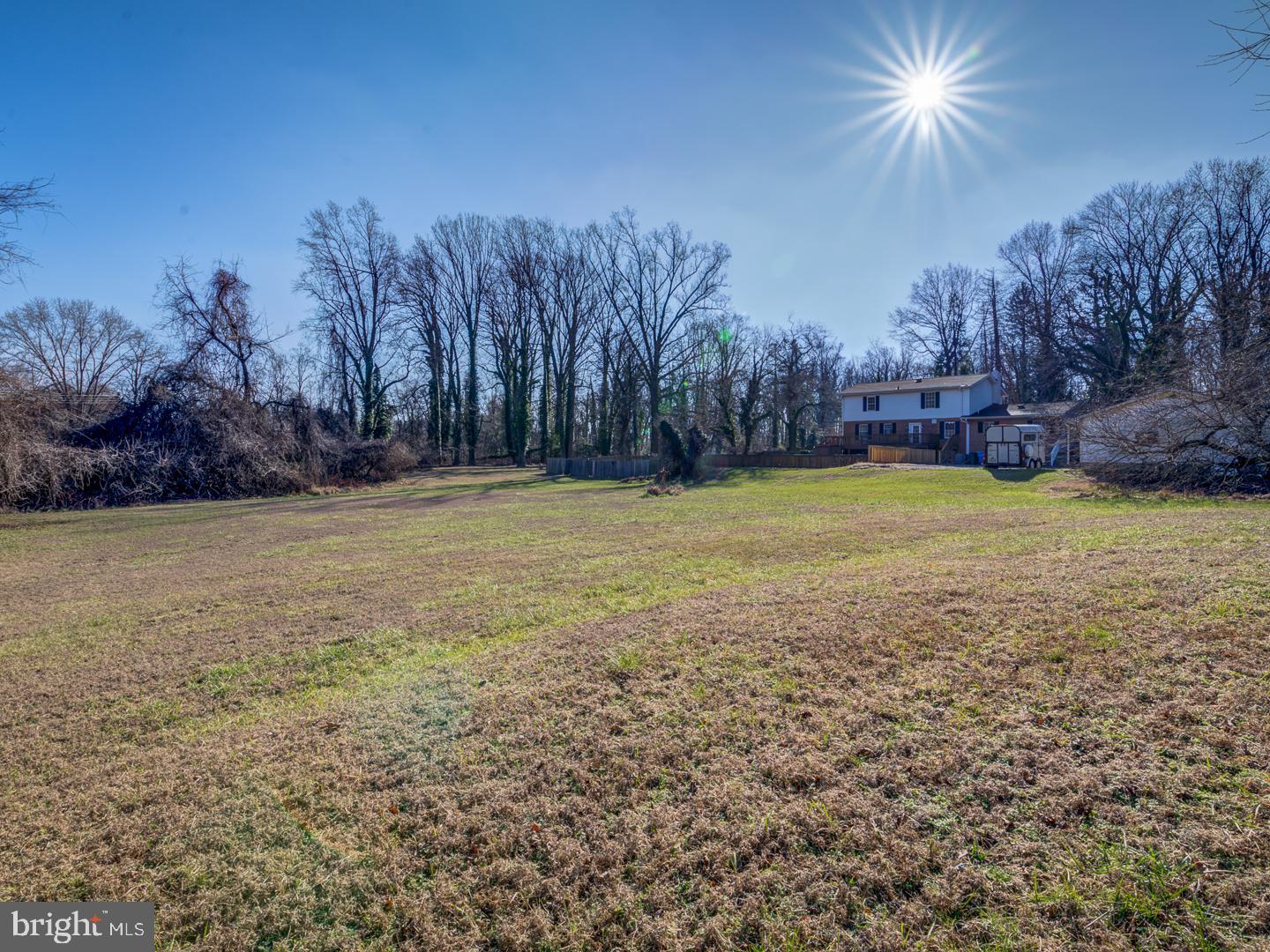 Large open yard with a two-story house, fencing, and leafless trees.