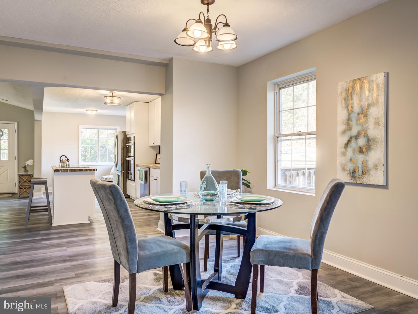 Dining area with a glass-top table and upholstered chairs, open to a white kitchen.