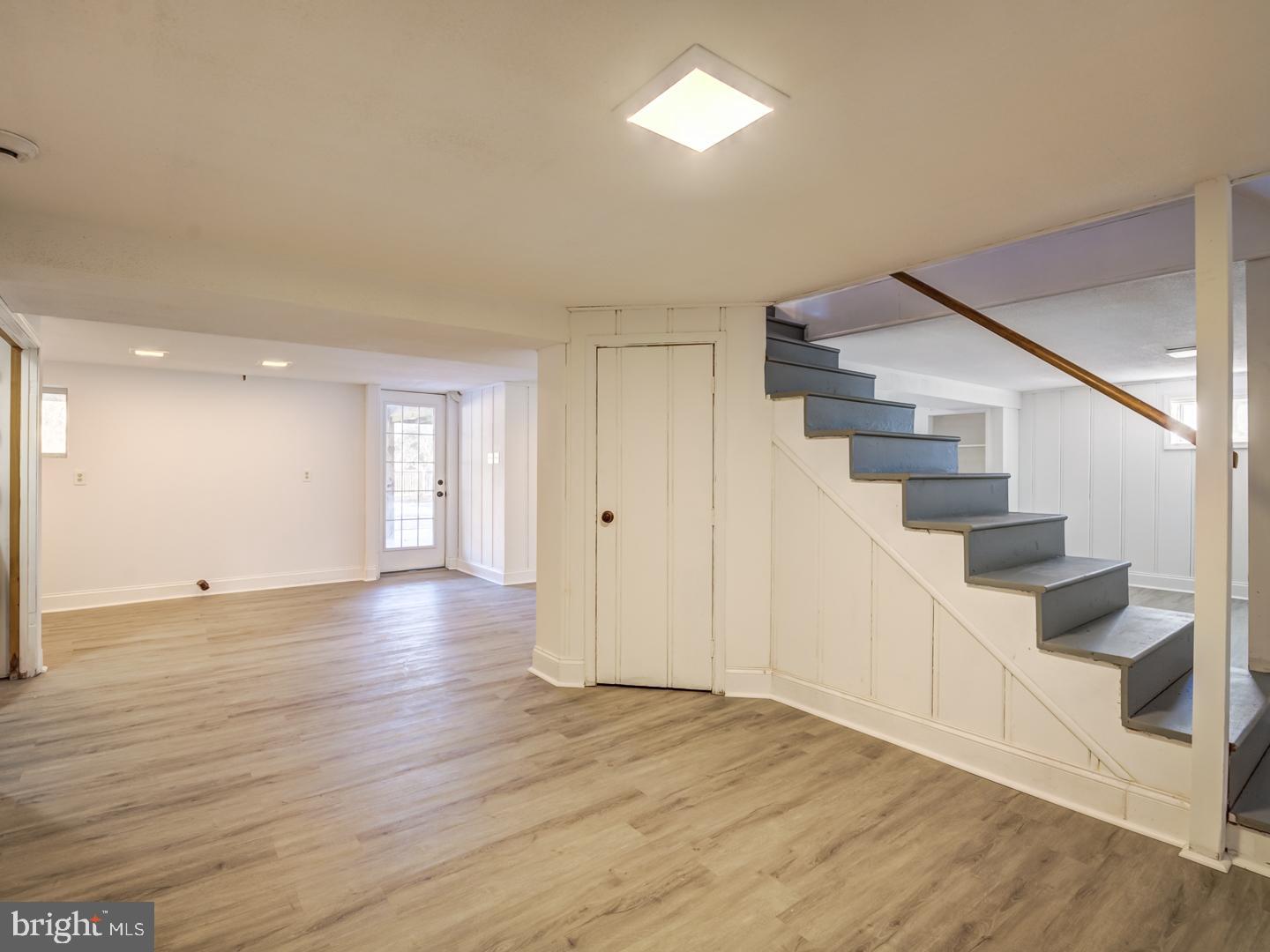 Unfurnished lower-level room with wood-look flooring and blue-gray stairs beside a central closet.