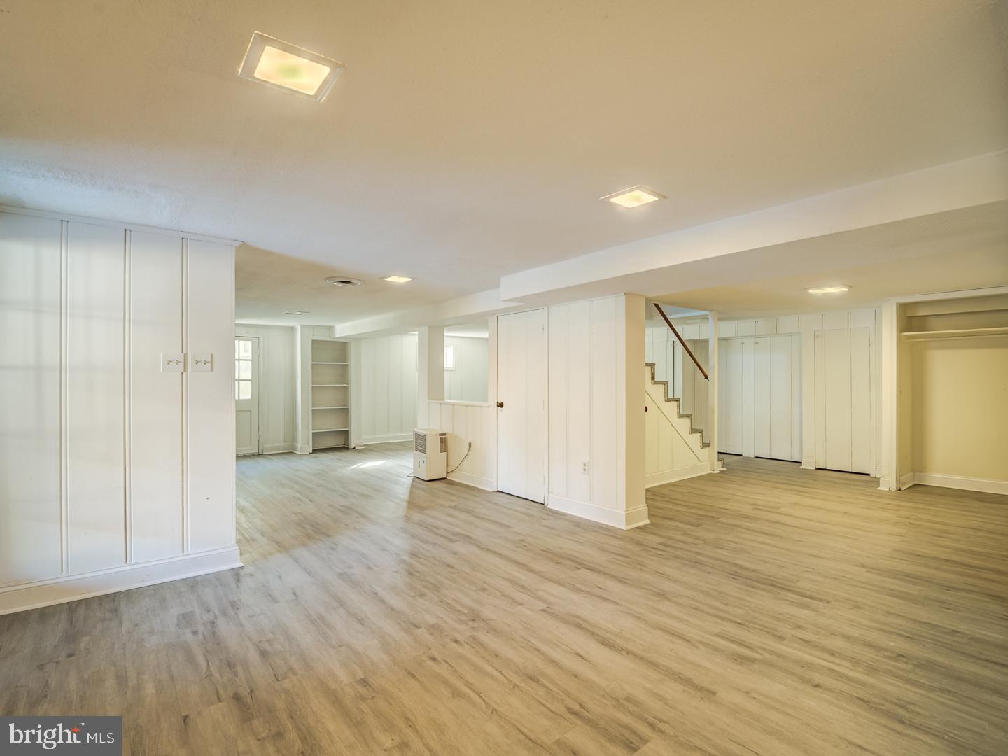 Vacant basement with gray plank flooring, built-in storage, and stairs.