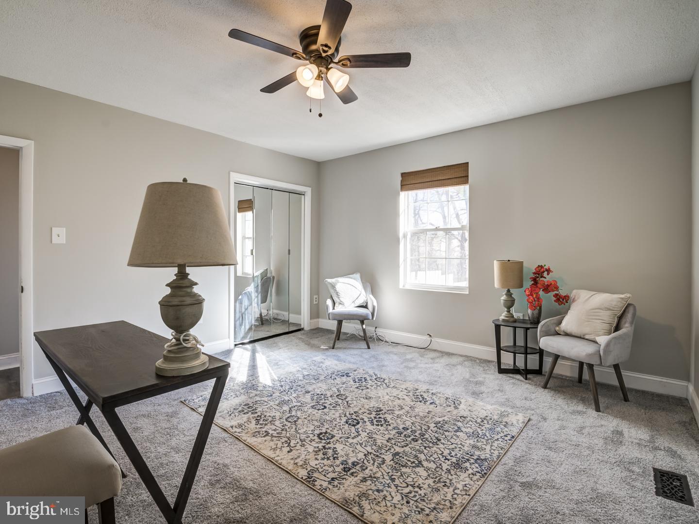 Furnished living room with mirrored closet doors, a patterned rug, and a ceiling fan.