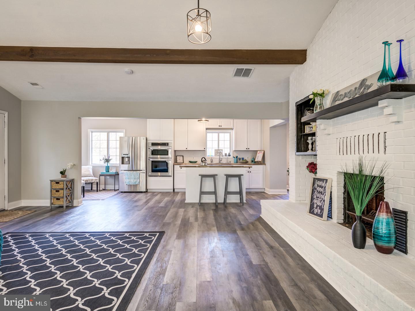 Open-plan kitchen and living room with a white brick fireplace, island seating, and stainless steel appliances.