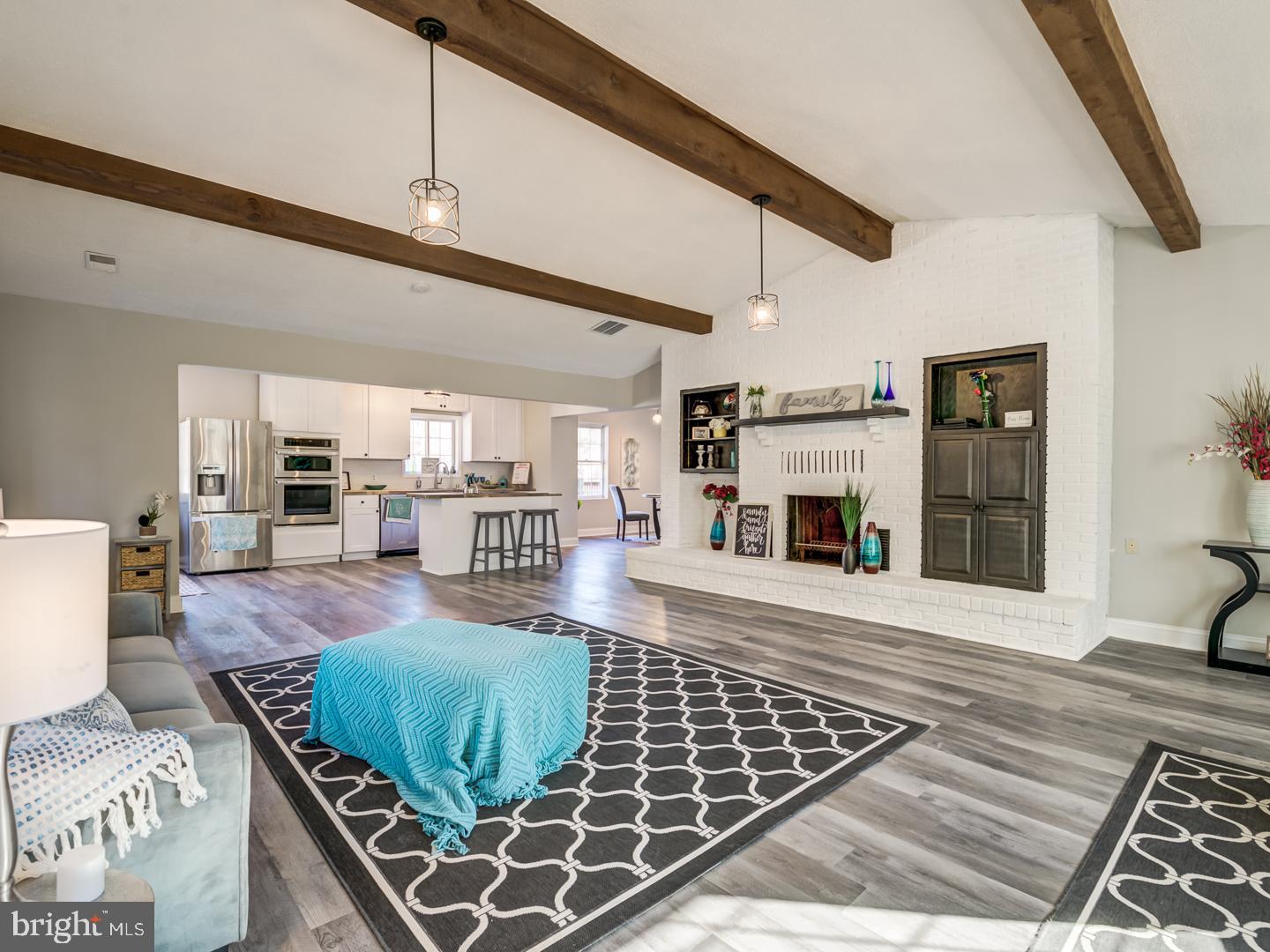 Open living room and kitchen with exposed beams, a white brick fireplace, and a breakfast island.