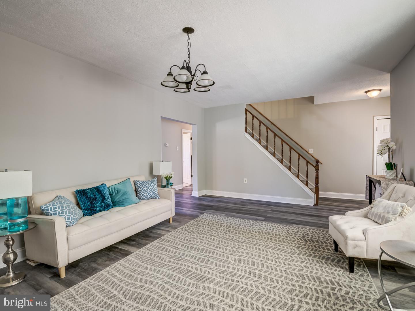 Living room with cream sofas, teal cushions, a large patterned rug, and a staircase.
