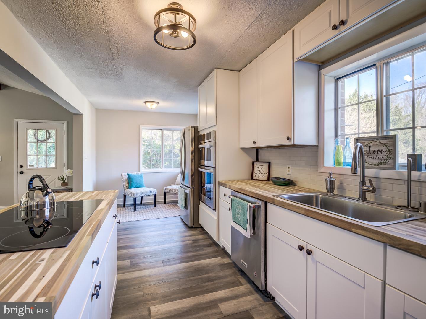 Bright kitchen with white cabinets, butcher-block counters, stainless appliances, and a window-side sink.