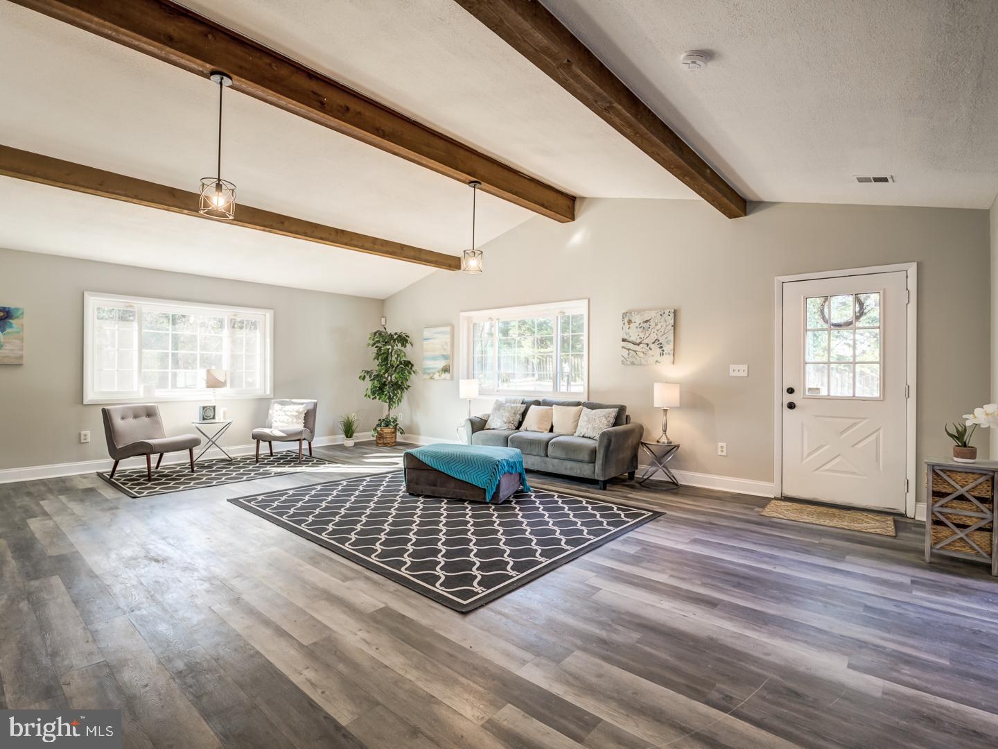 Staged living room with exposed wood ceiling beams, a gray sofa, accent chairs, and large windows.