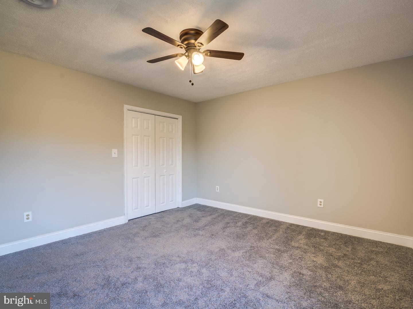 Empty bedroom with gray carpet, white closet doors, and a ceiling fan with lights.