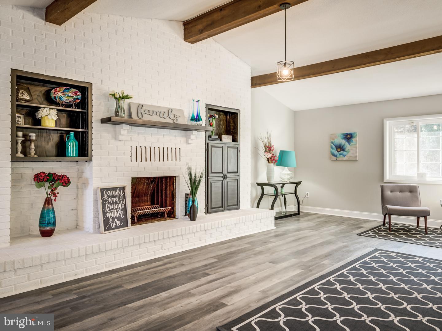 Living room with a white brick fireplace, built-in shelves, and exposed wood ceiling beams.