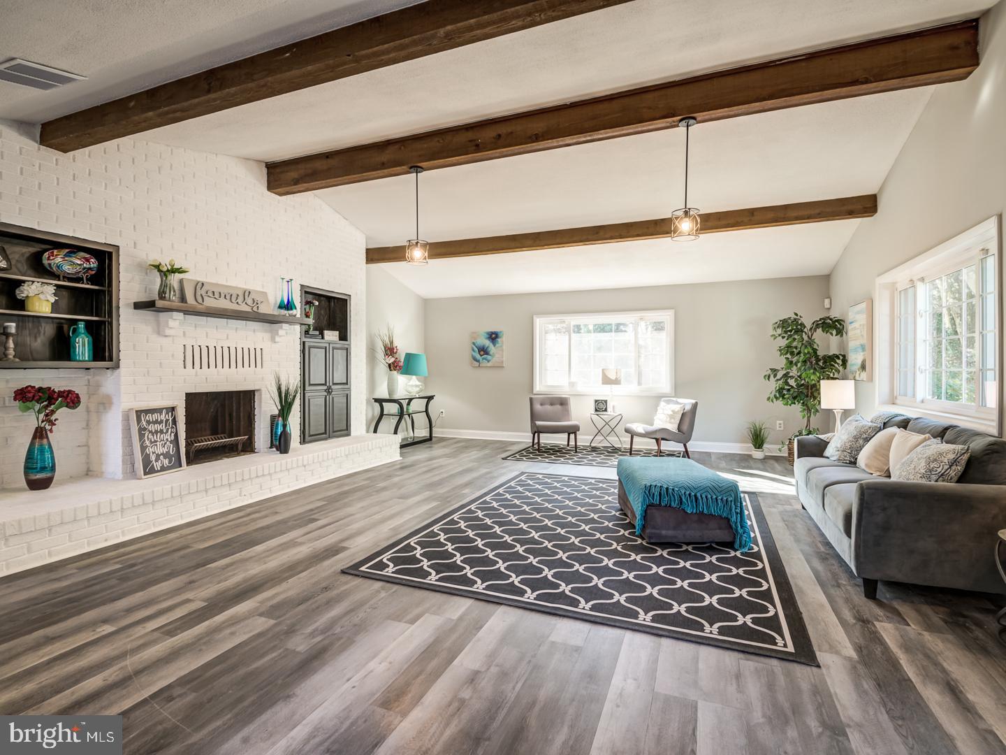 Living room with a white brick fireplace, exposed wood beams, and a patterned rug.