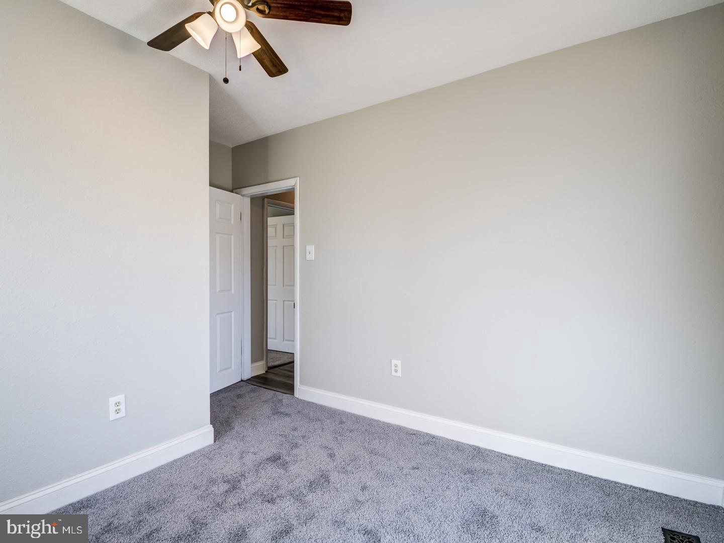 Empty carpeted bedroom with gray walls, an open doorway, and a ceiling fan with light.