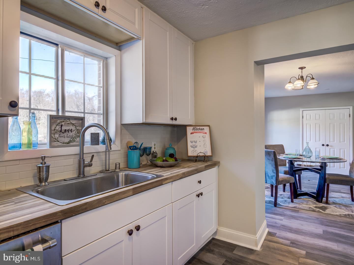 Kitchen with white cabinets, a stainless steel sink, and a window opening onto a furnished dining area.