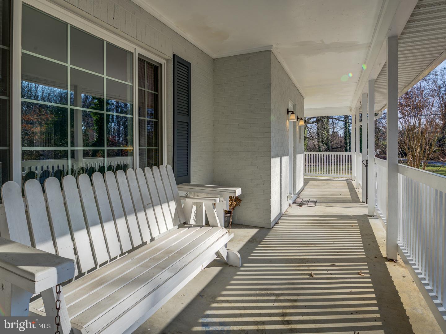 Covered front porch with white benches and railings, sunlight casting striped shadows across the floor.