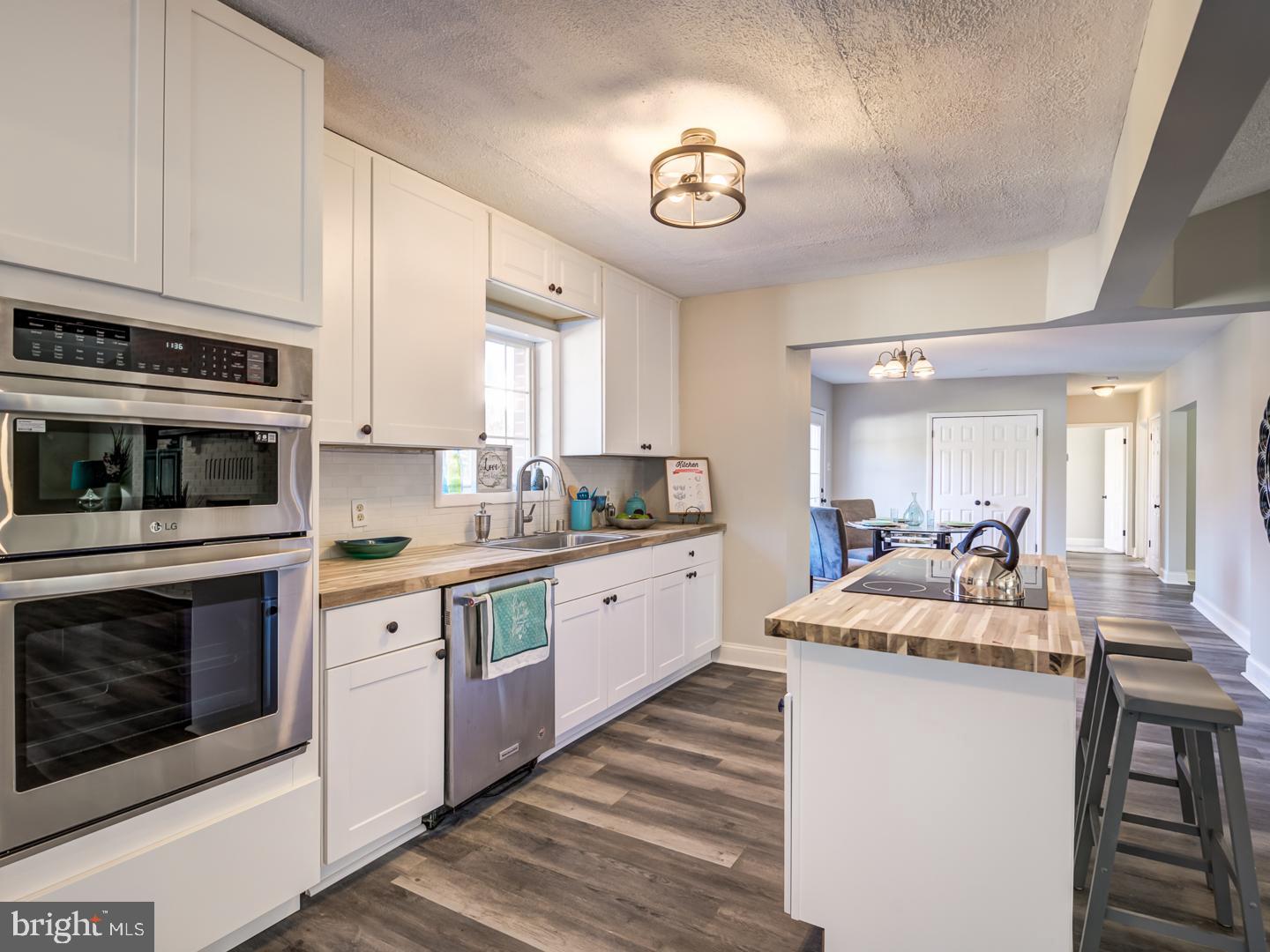 Kitchen with white cabinets, stainless steel double ovens, butcher-block counters, and a central cooktop island.
