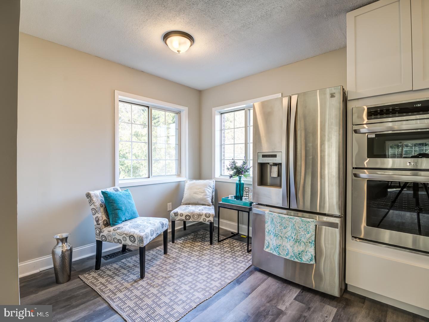 Kitchen with stainless steel appliances, two patterned chairs, and windows overlooking greenery.