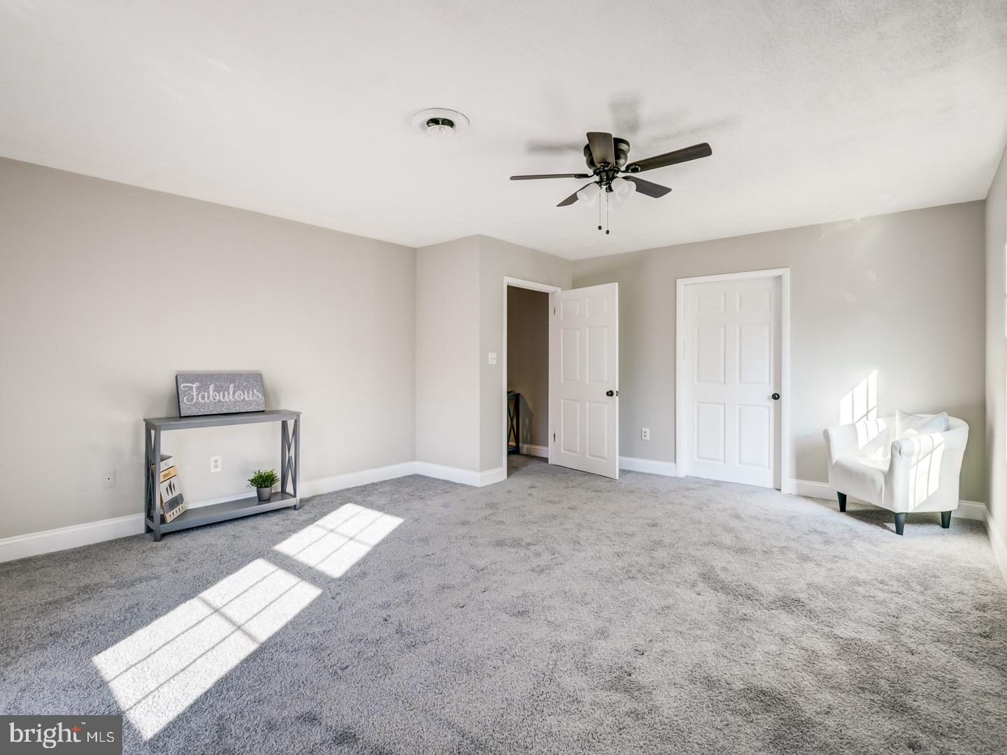Bright carpeted room with a ceiling fan, white armchair, and console table.