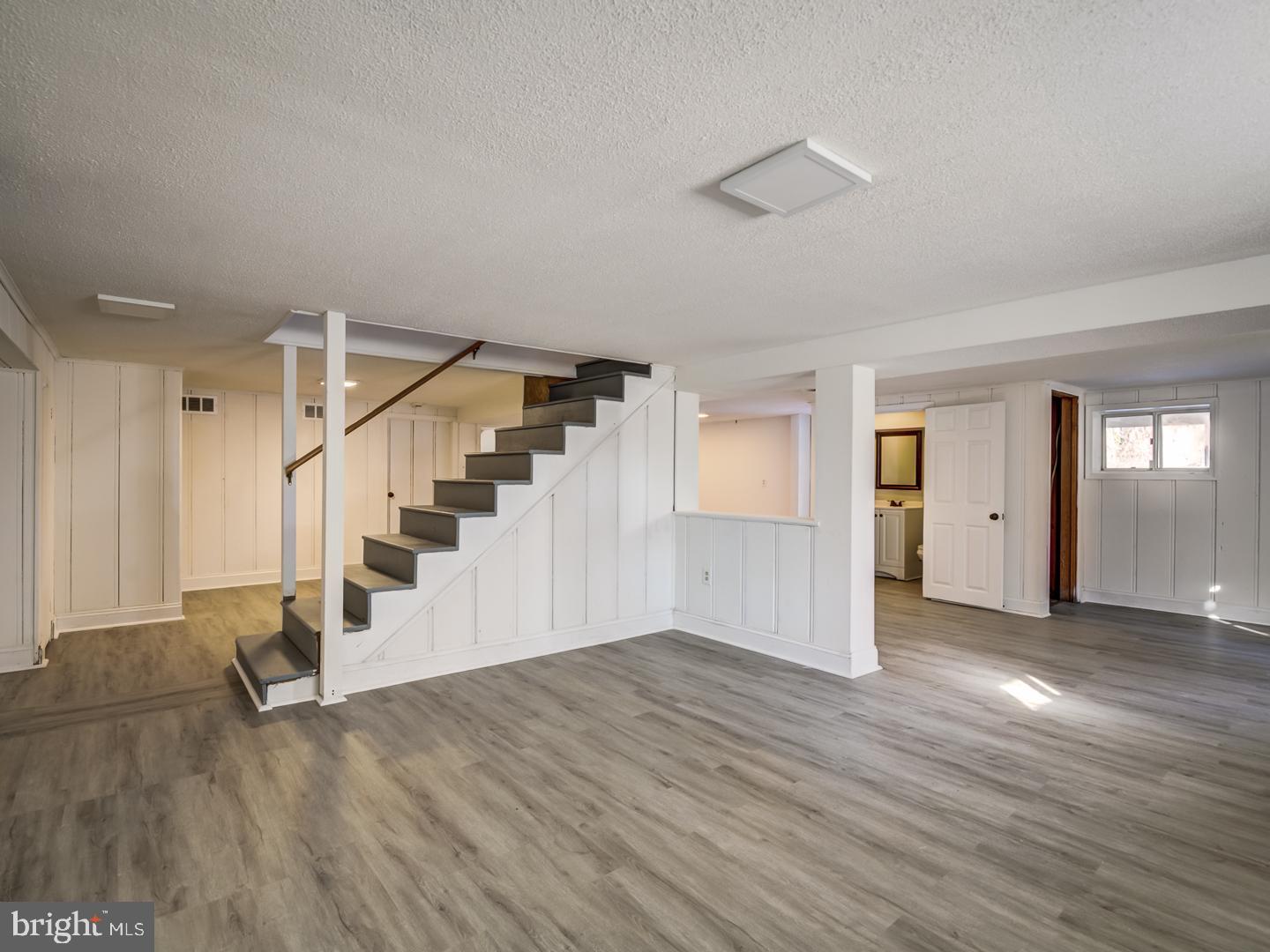 Finished lower-level recreation room with gray plank flooring and a central staircase.