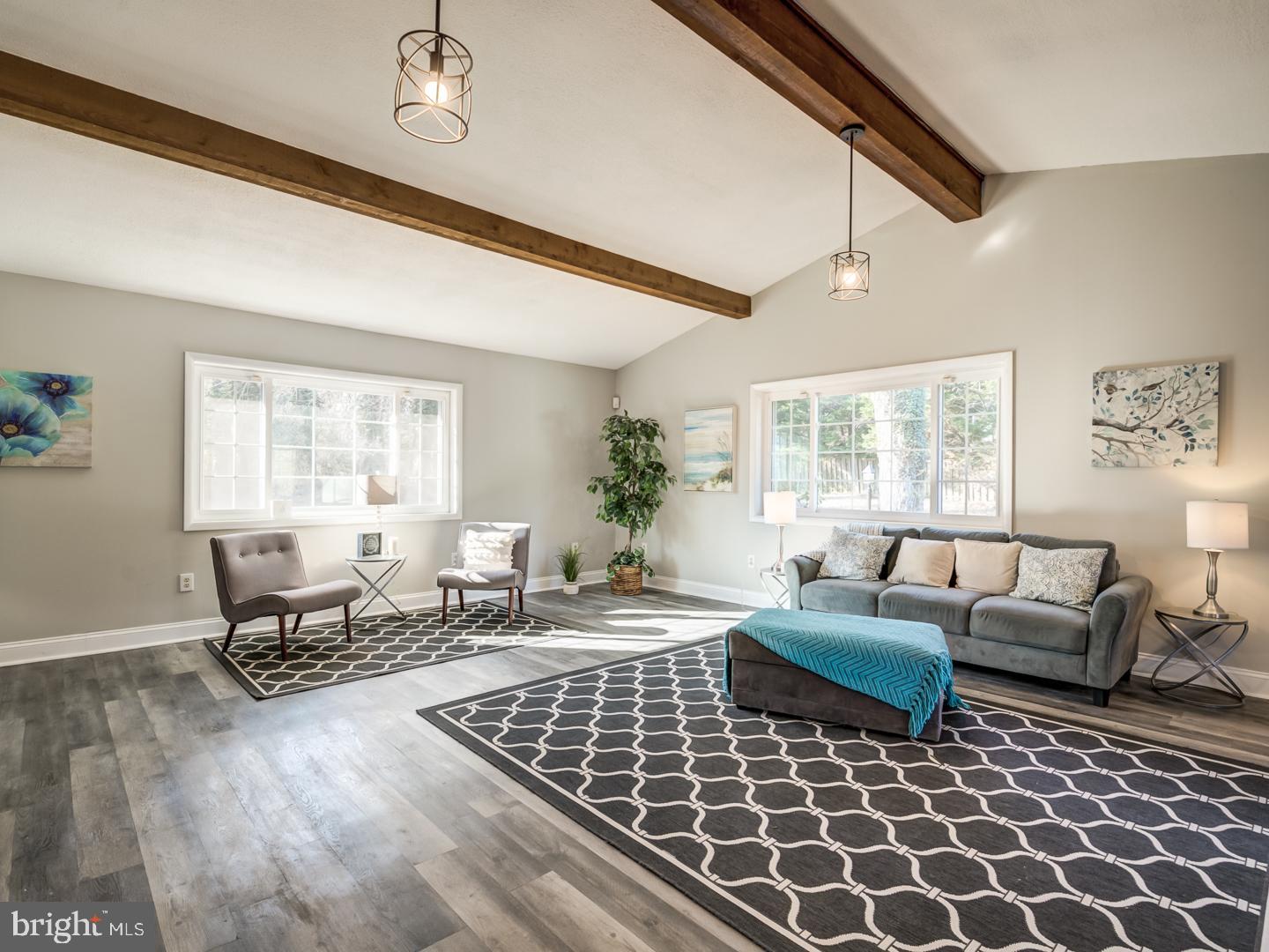 Staged living room with exposed ceiling beams, large windows, and gray seating.