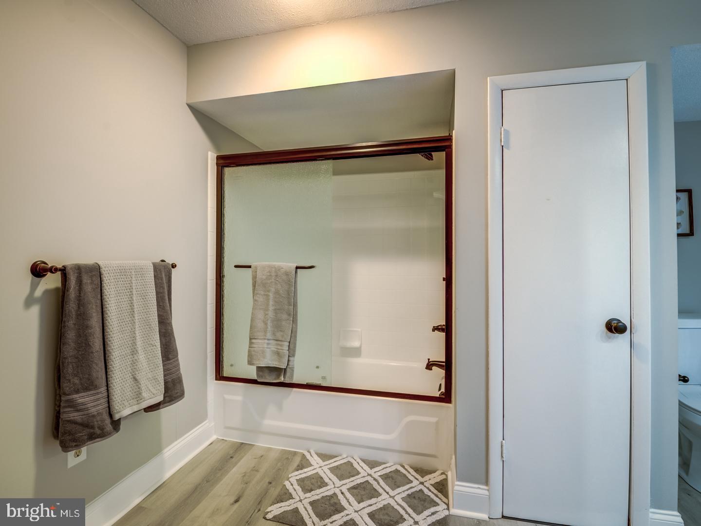 Bathroom with a glass-enclosed tub and shower, gray towels, and a patterned rug.