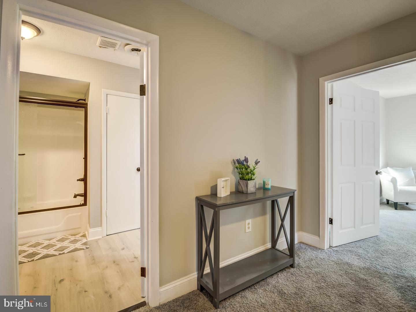 Hallway with a gray console table, opening to a bathroom and a carpeted sitting room.