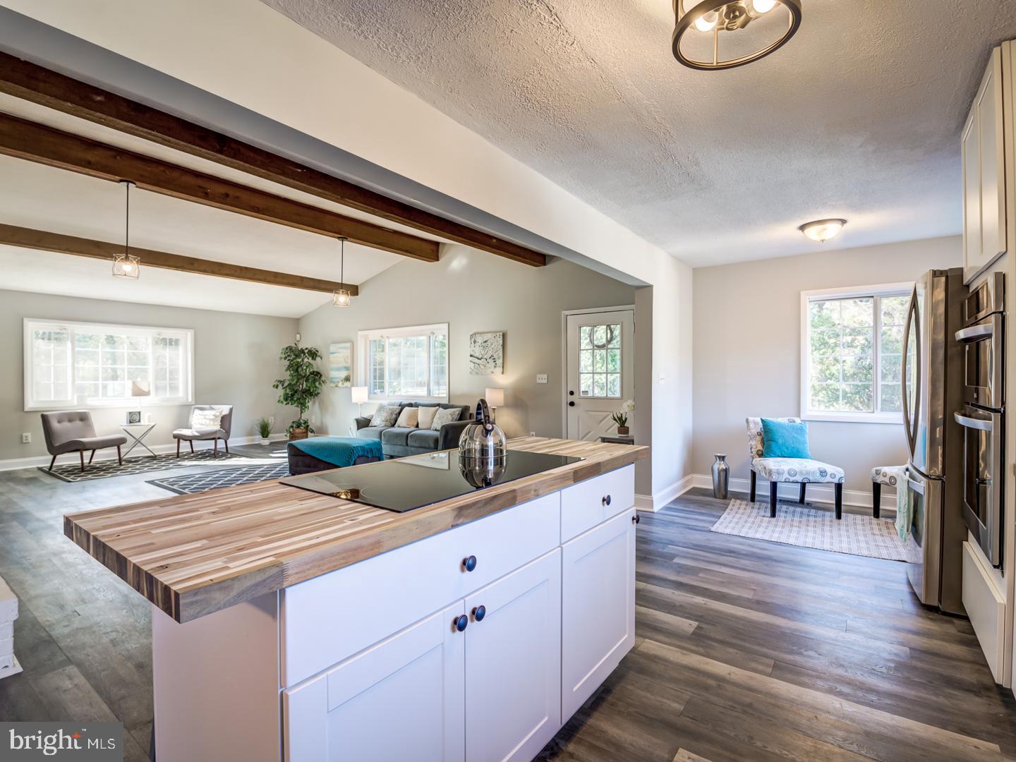 Open kitchen with a butcher-block island, black cooktop, exposed beams, and adjoining living area.