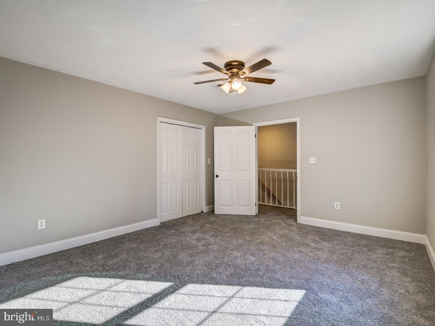 Unfurnished bedroom with gray carpet, a ceiling fan, and an open doorway to the stair landing.
