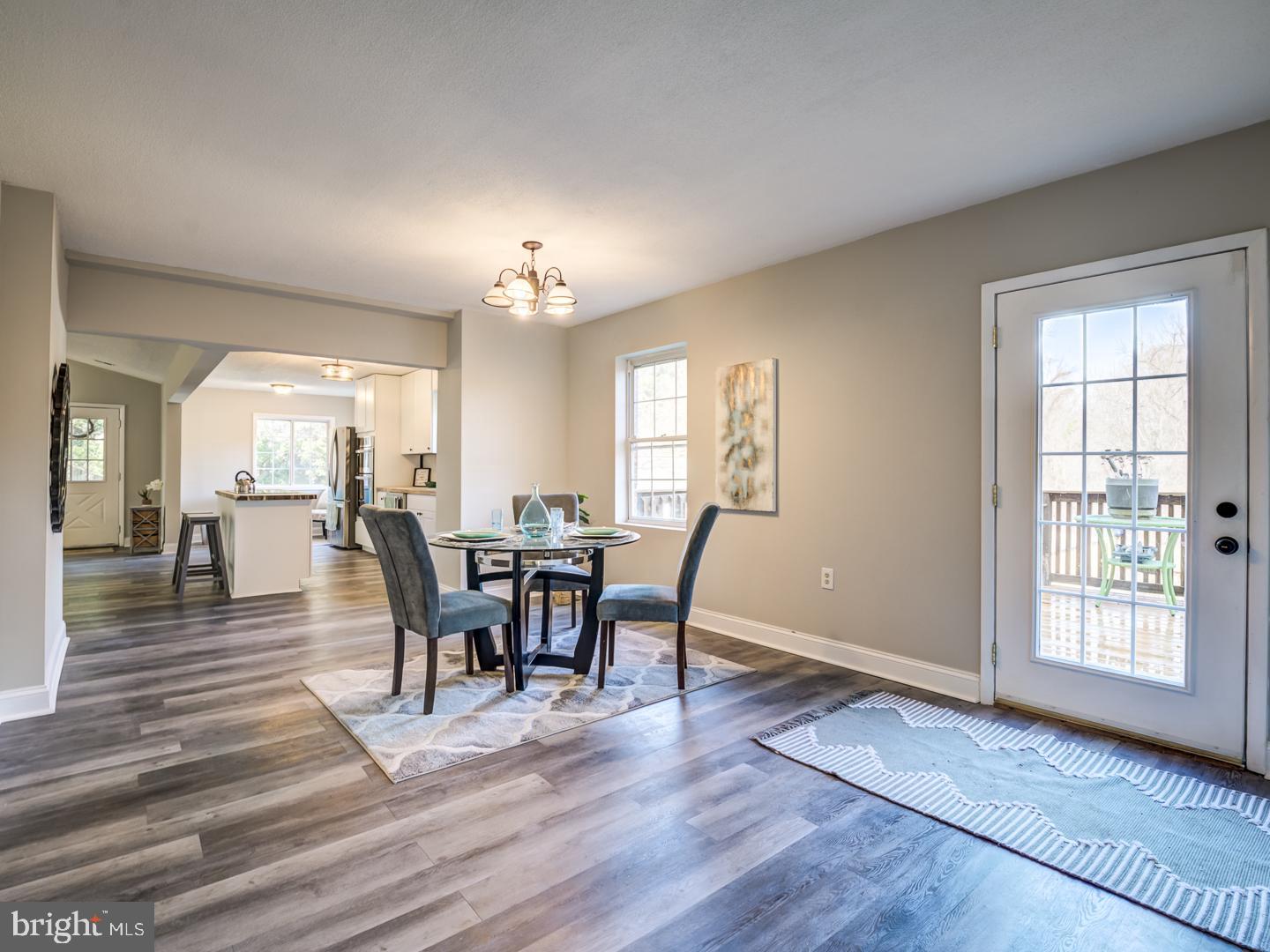 Dining area with a round table and chairs, opening into a bright kitchen beside a glass-paneled deck door.
