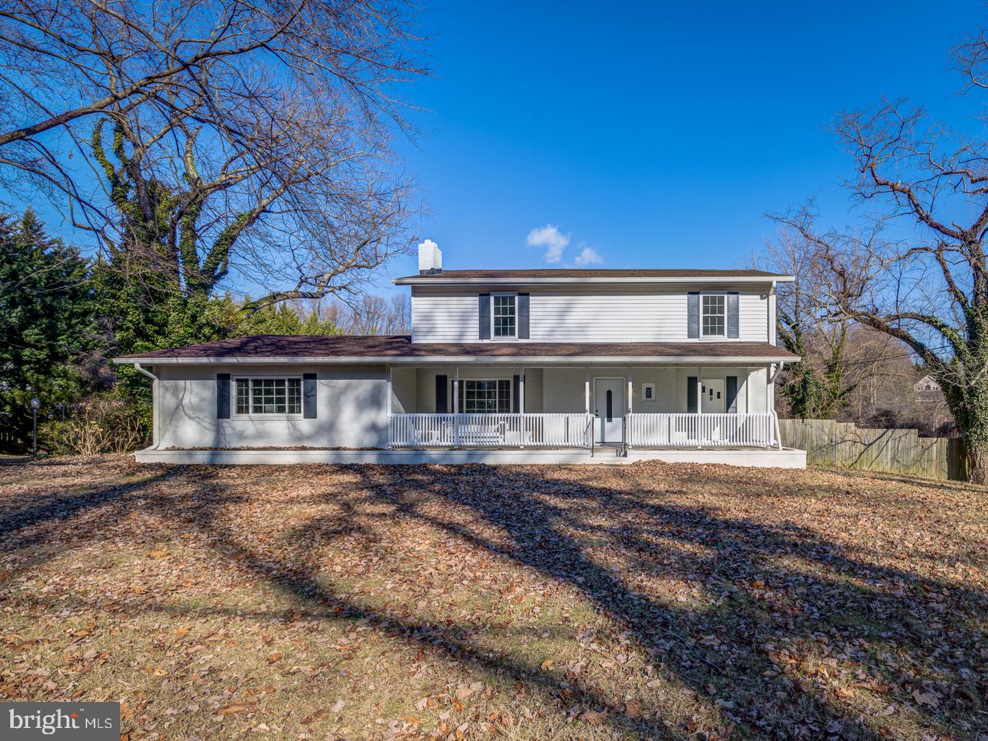 White two-story house with a long covered porch, dark shutters, and a leaf-covered yard.