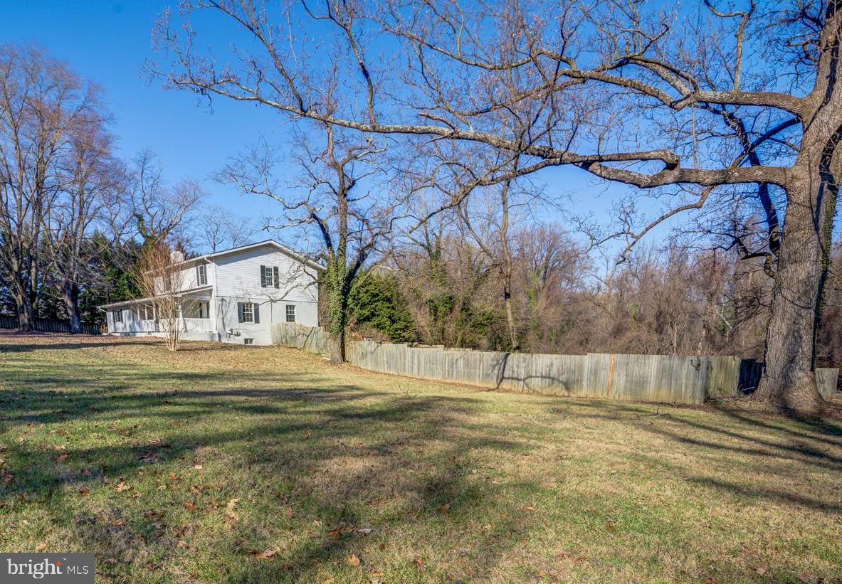 White two-story house beyond a broad fenced yard beneath leafless trees.