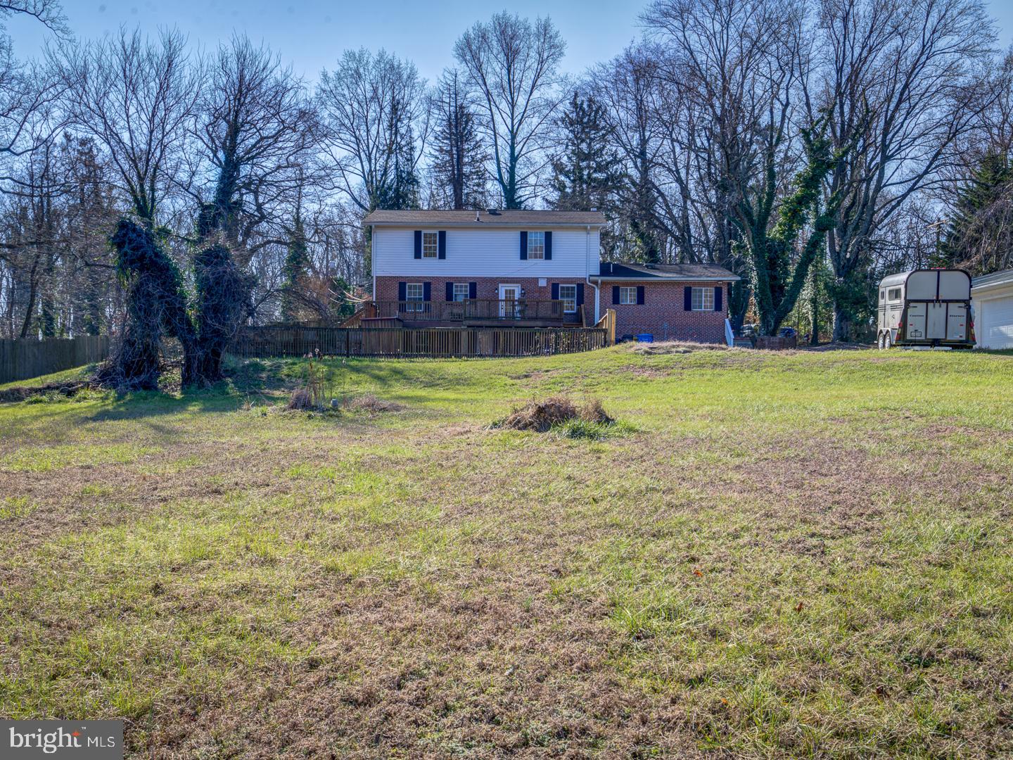 Rear of a two-story brick house with a wooden deck and fenced lawn.