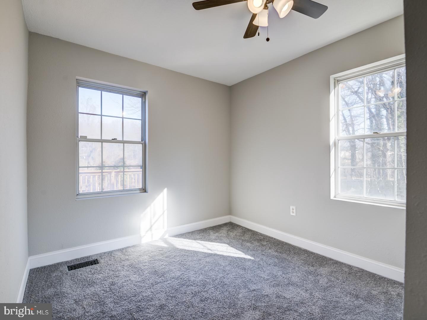Empty carpeted room with two windows and a ceiling fan.
