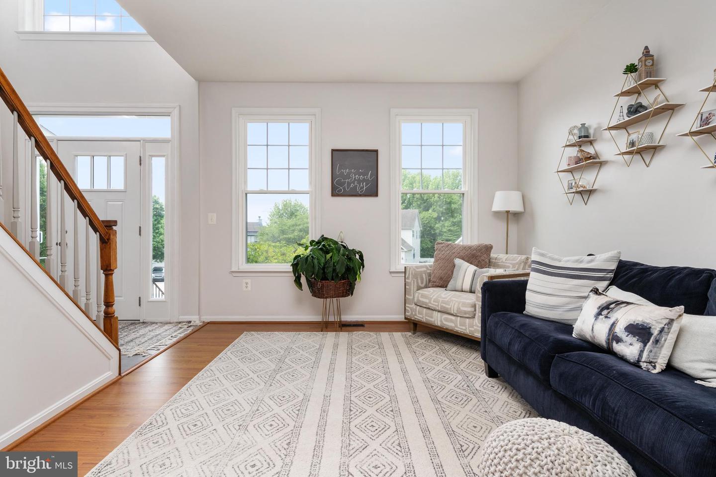 Staged living room with a navy sofa, geometric rug, and staircase with a wood handrail.