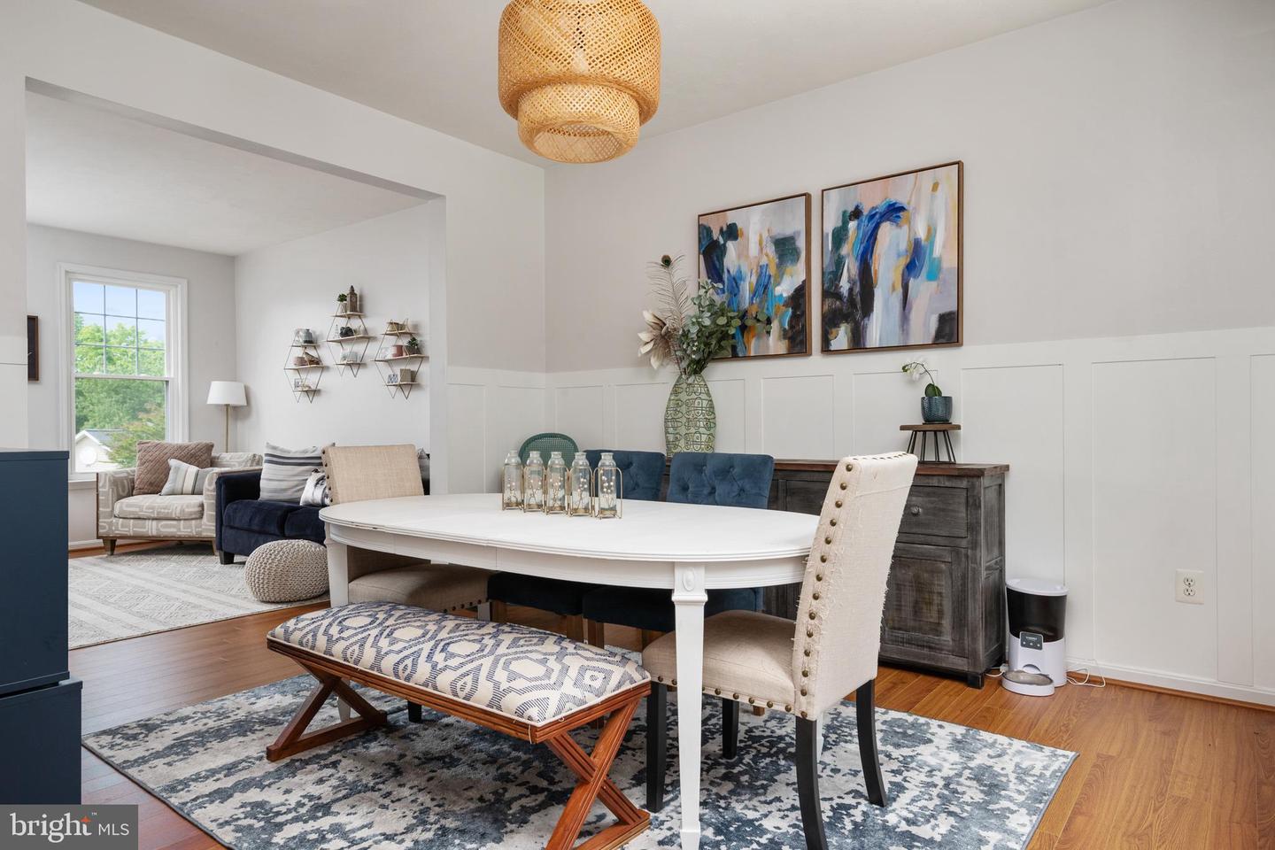 Staged dining room with a white table, upholstered seating, paneled walls, and an adjoining sitting area.