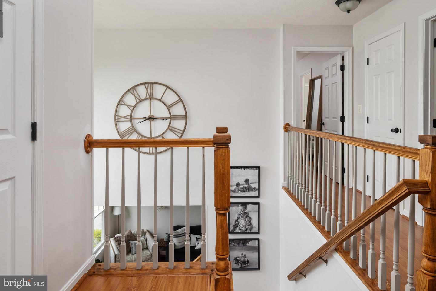 Upstairs landing with a large open-face clock and polished wood staircase railings overlooking the living room.