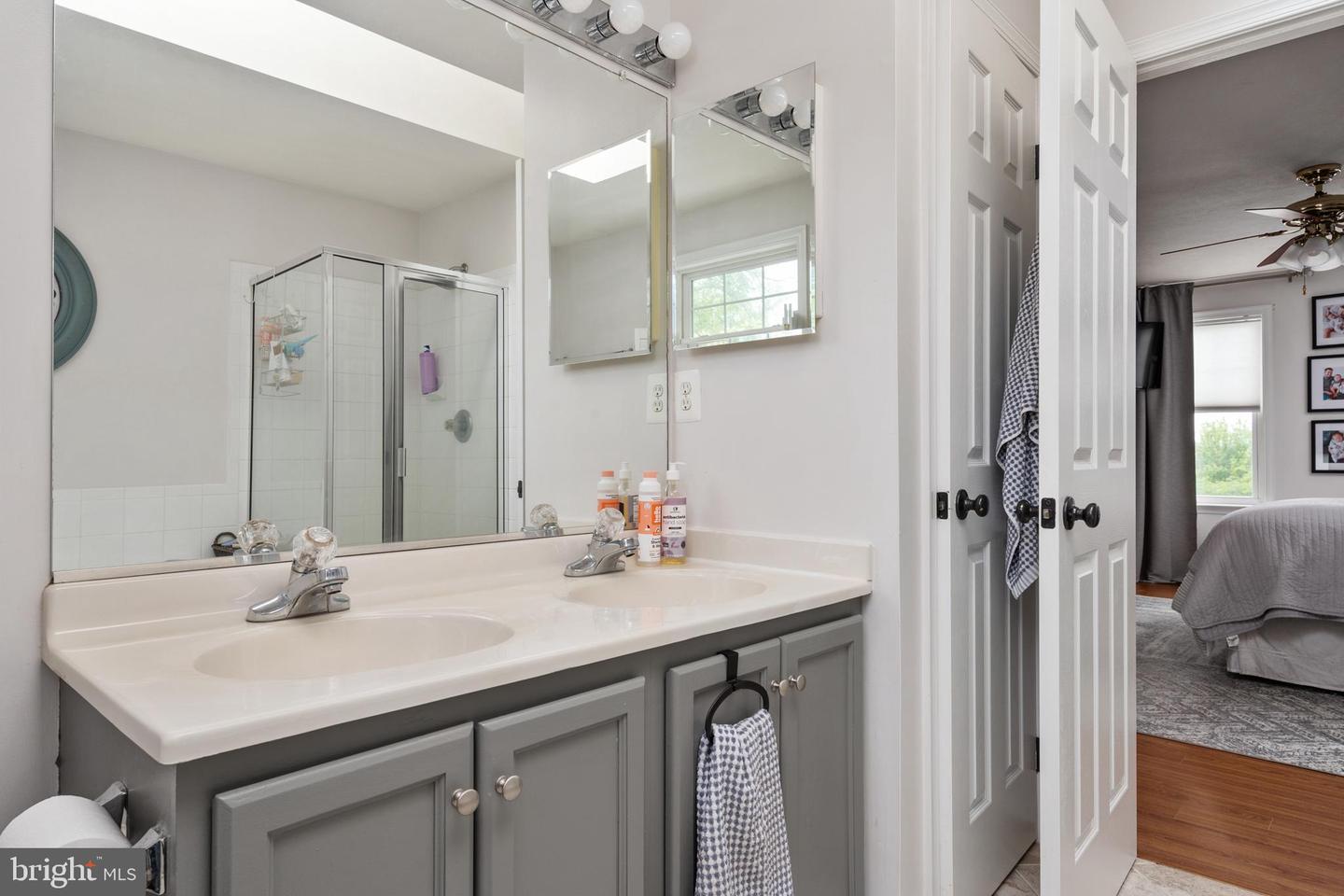 Bathroom with a gray double vanity, mirrored cabinets, and a glass-enclosed shower.