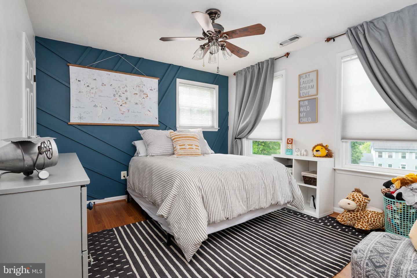 Bedroom with a teal geometric accent wall, striped bedding, gray curtains, and children’s toys.